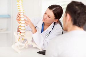 A doctor uses a model spine to show something to a patient.